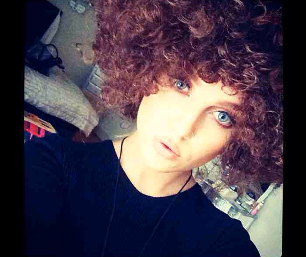 Perrie takes a temporary trip to the dark side and models a brown curly wig