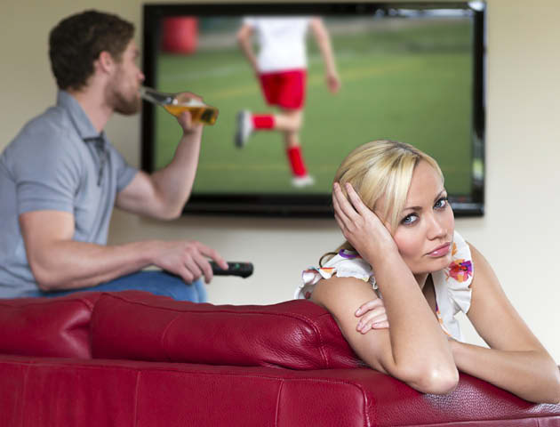 Woman looking bored while bloke watches football