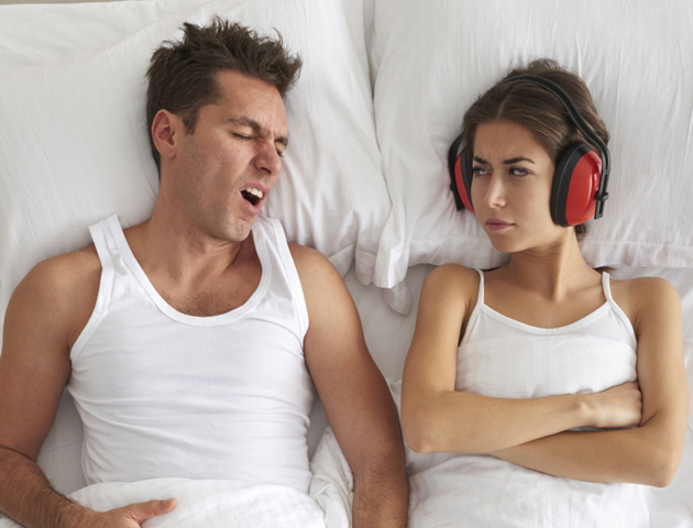 image of couple in bed- one snoring, one wearing ear protectors