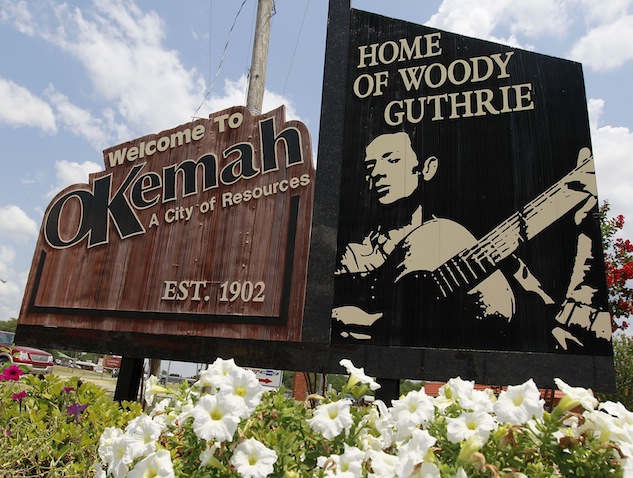 FILE - In this Friday, July 13, 2012 file photo, A sign welcomes people to Okemah, Oklahoma, the home of Woody Guthrie, in Okemah, Okla. A dispute over the finances and control of a planned rebuild of folk legend Woody Guthrie’s boyhood home in Oklahoma could put the project in jeopardy. (AP Photo/Sue Ogrocki, File)