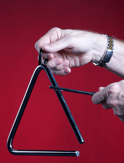 A musical triangle being played by hands isolated against a red background in the square format with copy space.