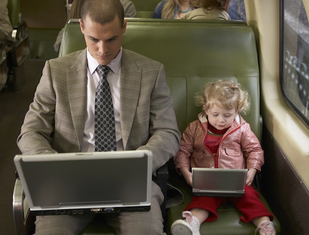 Man and toddler sitting on train on laptops