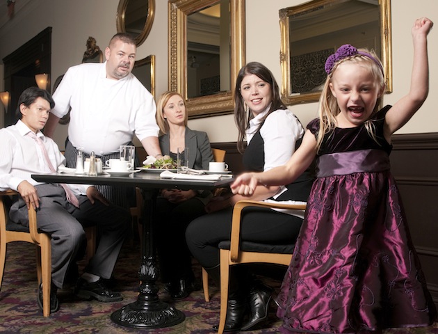 A little girl is acting up in a restaurant while diners look on.