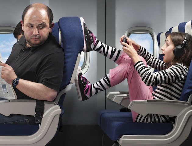 A carefree young girl annoying the passenger infront by pushing his seat.