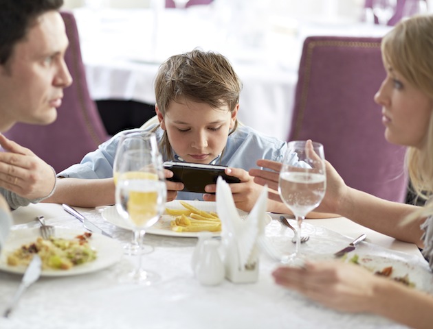 Little boy playing video games while having dinner with his parents