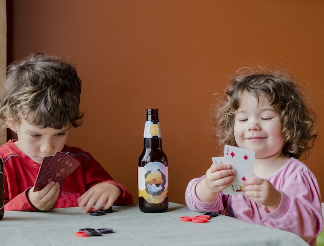 Two small children playing poker with bottle of beem