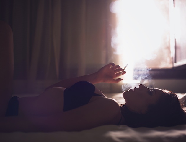 Beautiful girl smoking on the bed, backlit scene.