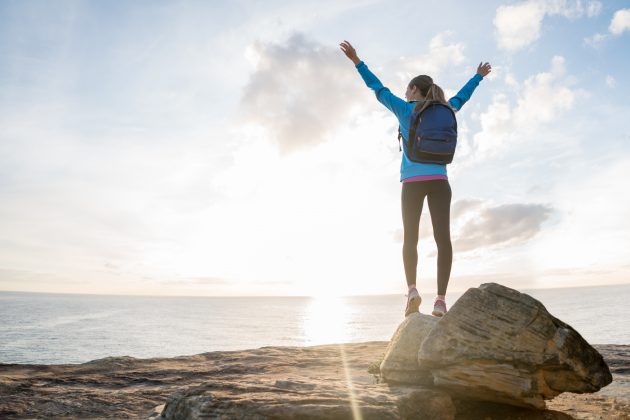 Happy hiker reaching the top of a mountain and standing with arms up watching the sunset