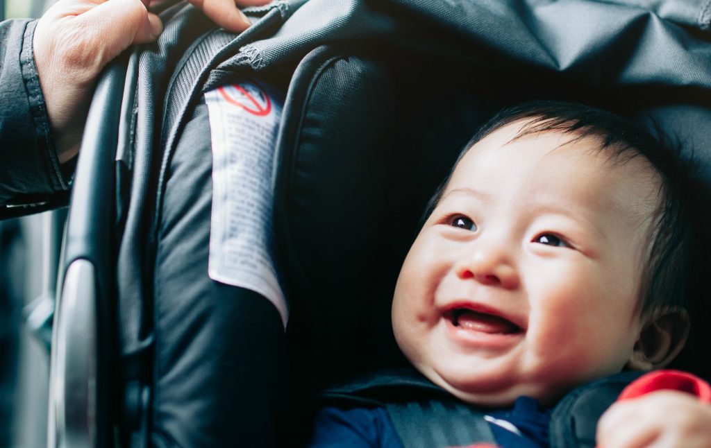 Close up of mother taking care of cute smiling baby on car seat in car