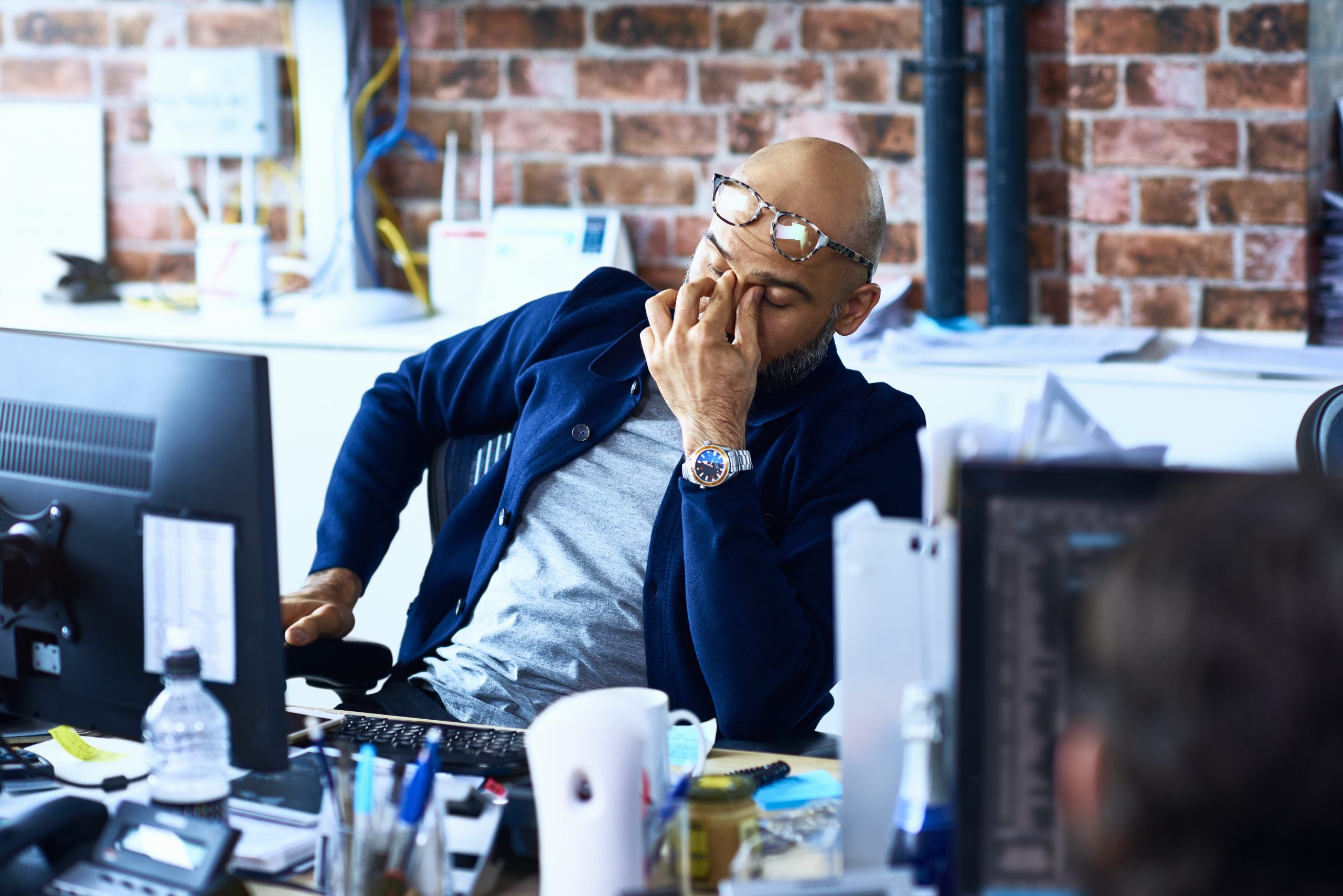 A tired man sitting at his desk at work wondering why am I always tired?