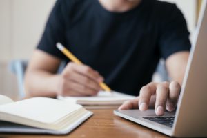 man studying with laptop and note pad - autumn exam retakes 2020