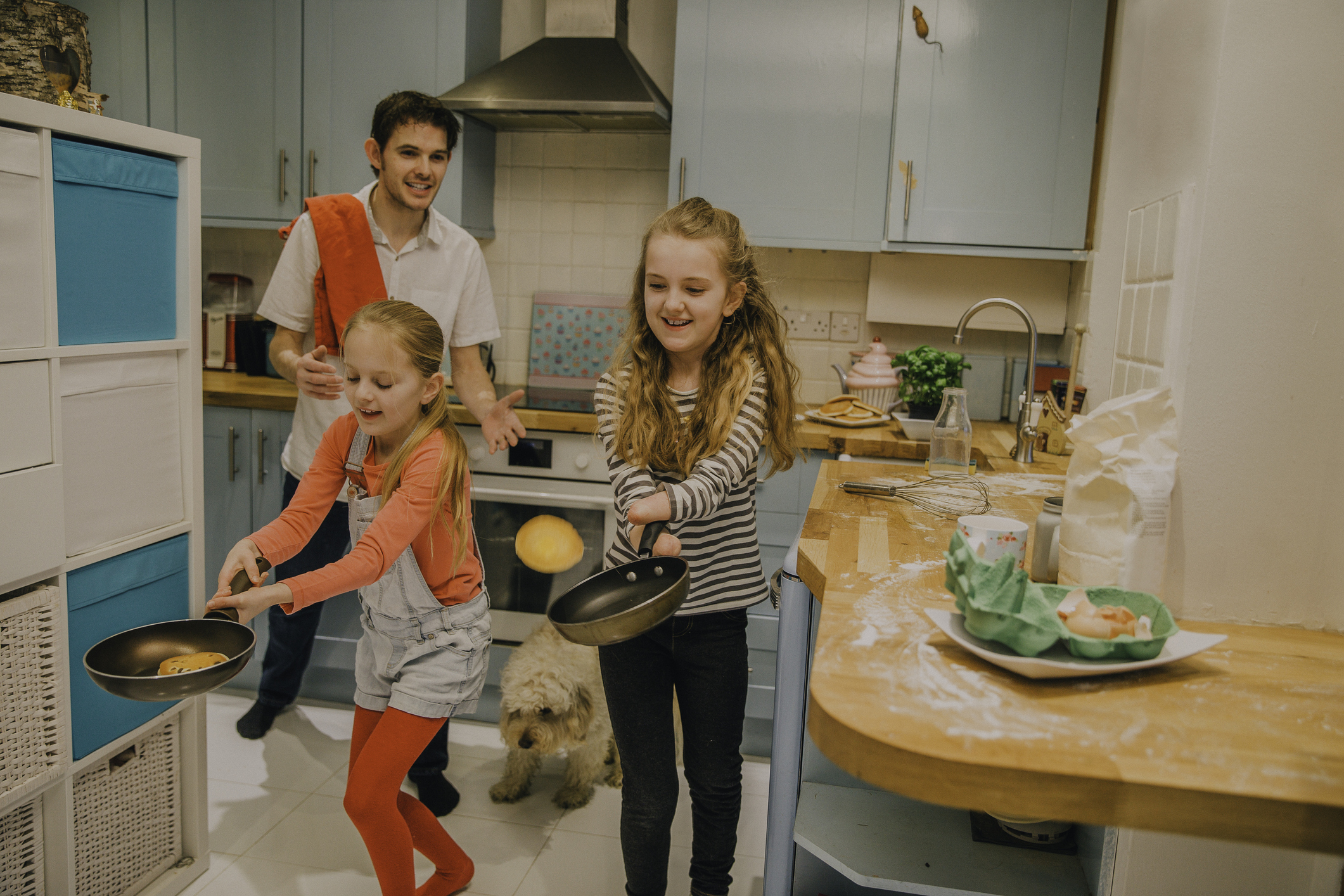 A father showing his daughters how to flip pancakes on Pancake Day.