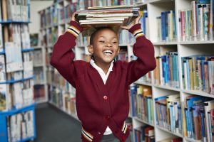 girl in library carrying books and smiling - when do English schools go back
