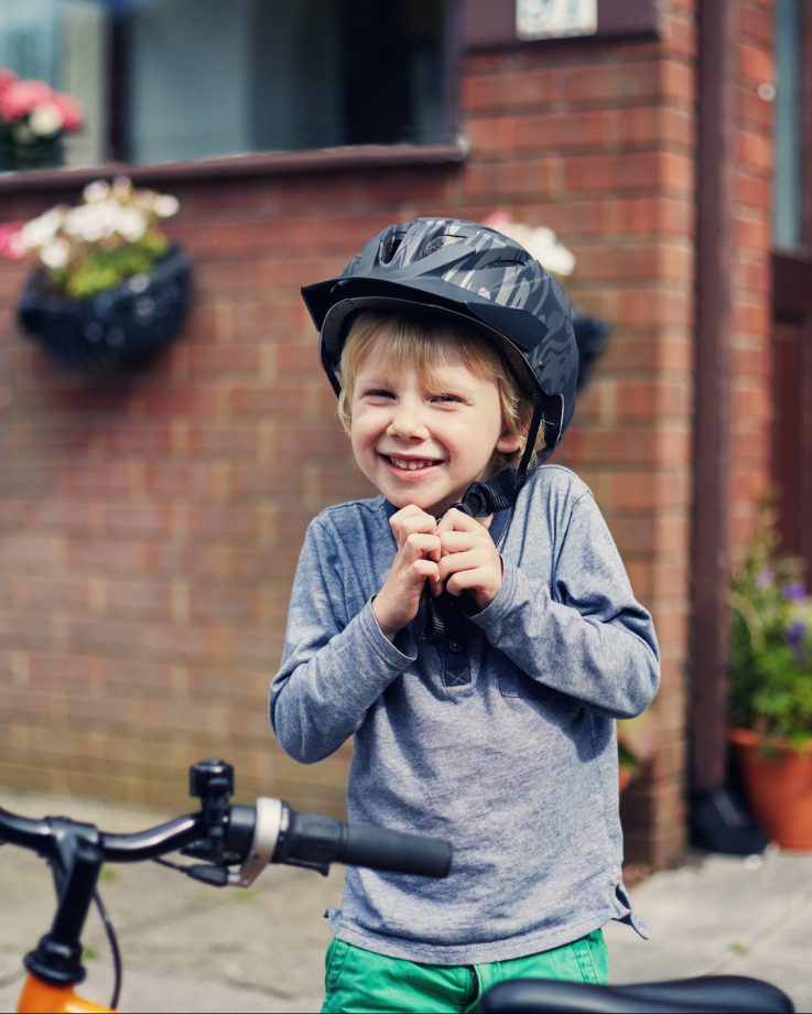 Happy little boy putting on a bicycle helmet