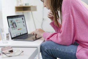 Young woman sitting on the couch using laptop to shop Black Friday vs. Cyber Monday deals