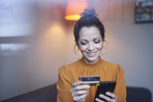 Smiling woman using smartphone and credit card at home for when Cyber Monday sales start