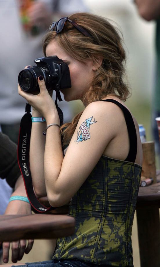 Emma Watson Takes Photos Backstage With A Comical Temporary Tattoo On Her Arm At Glastonbury 2010